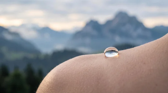 Gros plan délicat sur une goutte d'eau posée sur une peau saine, évoquant la douceur du renouvellement cellulaire dans un cadre alpin